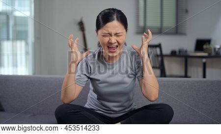 Asian Woman Angry And Shouting Sitting On Sofa At Home.