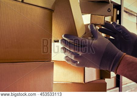 A Worker Man Hands Hold Cardboard Boxes On The Shelves Of A Fully Stocked Warehouse. Warehouse Overf