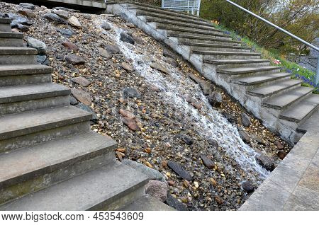 Between The Stairs Is A Waterfall With Stones And Boulders. Artificial Stream With A Waterfall Betwe
