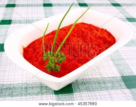 Jasně červený Ajvar v bílé misce s pažitkou a petrželkou