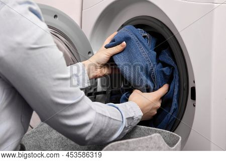 Woman In Light-colored Shirt Pulls Dirty Denim Out Soft Basket And Puts Them In Drum Of Washing Mach