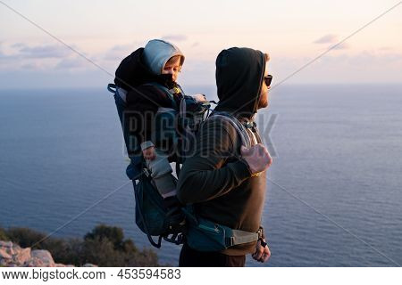 Young Caucasian Man Hiking Near Beautiful Blue Sea Carrying Baby In Bacpack, Sling, Carrier.family T