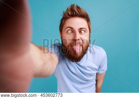 Portrait Of Handsome Childish Bearded Man Blogger Making Point Of View Phone, Showing Tongue Out, De