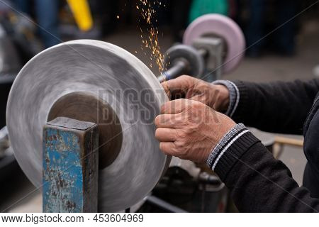 Man Holding In Hands Axe Closeup And Using Sharpening Machine. Senior Man Hands Sharpening Rusty Axe