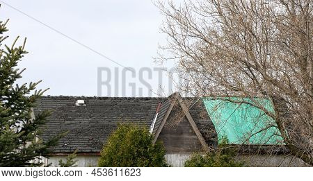 Residential Roof In Desperate Need Of Repair Or Replacement With Peeling Shingles And Tarp
