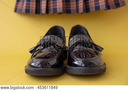 Black Patent Leather Loafers And A Plaid Scottish School Skirt In The Background On A Yellow Backgro