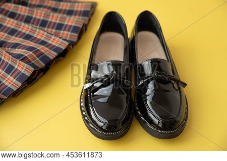 Black Patent Leather Loafers And A Plaid Scottish School Skirt On A Yellow Background.