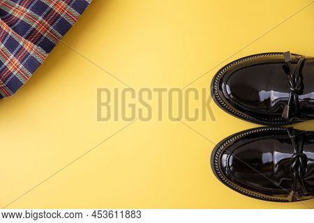 Black Patent Leather Loafers And A Plaid Scottish School Skirt On A Yellow Background Place For Text