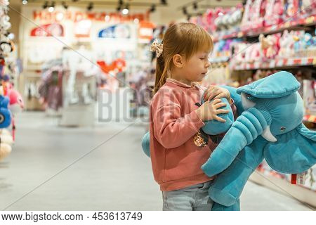 Little Caucasian Girl Coosing A New Toy In The Big Baby Store.