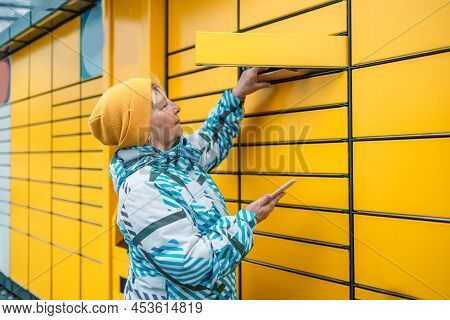 Caucasian Woman Picks Up Mail From Automated Self-service Post Terminal Machine. Mail Shipping Conce
