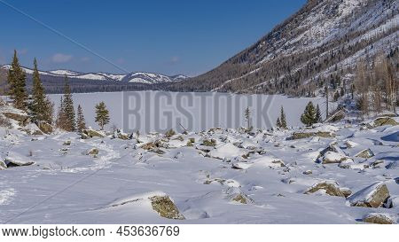 The Frozen Lake Is Surrounded By Mountains. Smooth Clean Snow On The Surface. Coniferous Trees, Cobb