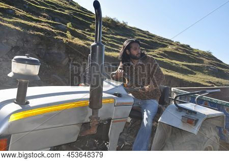 A Good Looking Bearded And Long Haired Young Guy Looking Sideways While Driving An Old Tractor In Th
