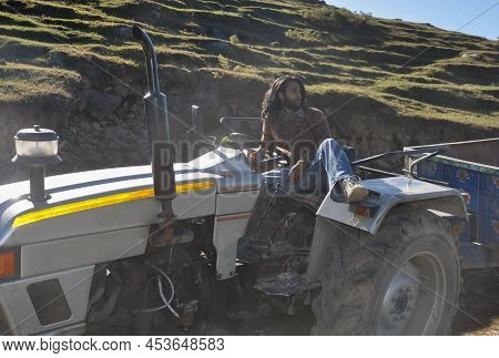 A Sexy Bearded And Long Haired Young Guy Looking Away While Posing With Sitting On An Old Tractor In