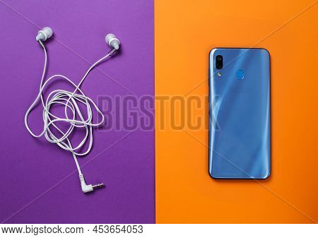 A Modern Blue Phone On An Orange Background And Headphones On A Purple Background.
