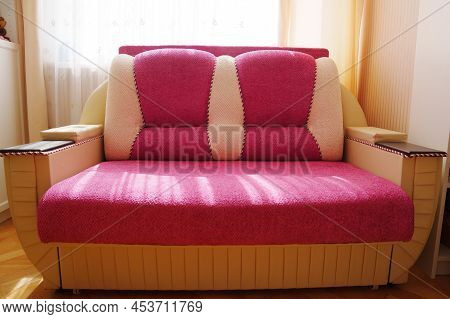 Sofa Bed Made Of Pink Fabric With Wooden Armrests.