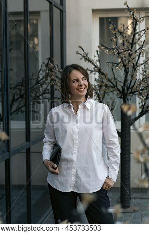 Portrait Of Successful Young Woman In White Shirt And Black Trousers. Business Woman In Semi-casual