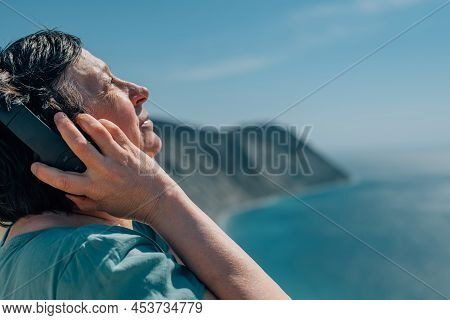 Portrait Adult Woman Listens To Music In Headphones In Summer, Spring Against The Backdrop Of Mounta