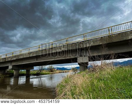 Concrete Bridge Over Olt River At Early Spring, Forming Stormclouds In Transylvania, Romania.