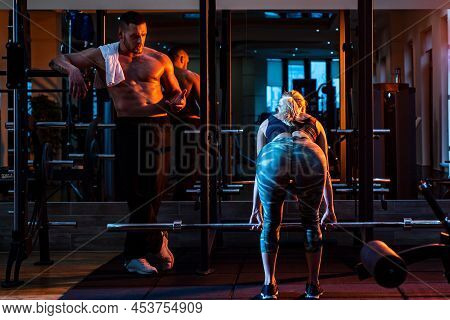 Couple Training With Barbell In Gym. Muscular Trainer Man Training Woman With Barbell.