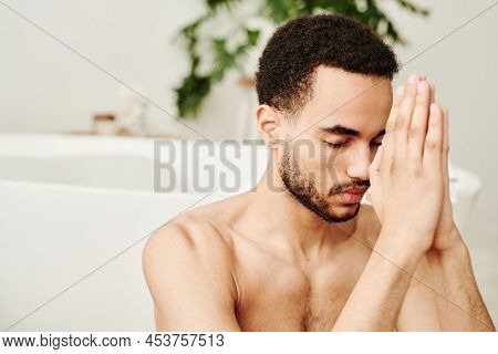 Young Man Sitting With Eyes Closed And Meditating During Yoga At Home