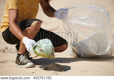 Volunteer Collecting Garbage Left By Tourists On Sandy Beach