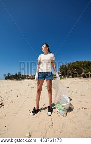 Asian Young Woman In Denim Shorts Picking Up Trash On Beach On Earth Day
