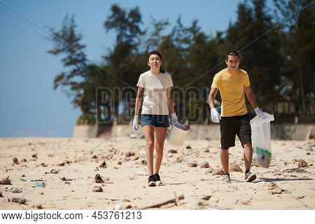 Young Couple Walking On Sandy Beach And Picking Up Trash On Dirty Beach