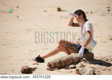 Tired Young Woman Sitting On Palm Truck After Picking Up Trash On Beach On Earth Day