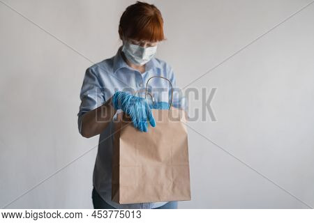 The Girl In The Means Of Individual Protection Sadly Looks Into An Empty Paper Bag. Lack Of Food, Hu