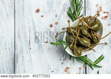 Capers. Marinated Or Pickled Canned Capers Fruit With Fresh Rosemary In A Small Bowl, On Light Woode