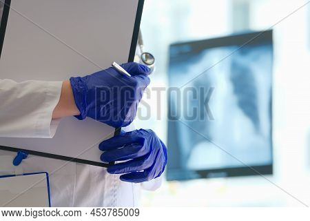 Doctor Is Holding Clipboard And Pen In Background Of X-ray Of Lungs. X-ray Of Lungs In Pneumonia Con