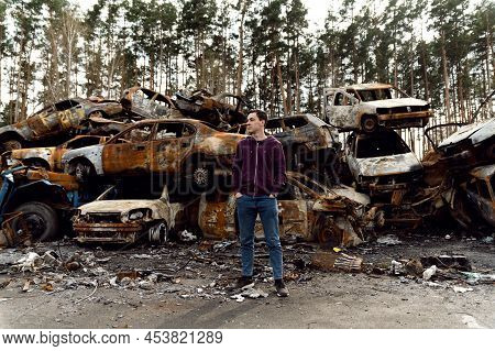 Ukrainian Man Stands Against The Background Of Broken And Burnt Cars Affected By Russian Missiles. D