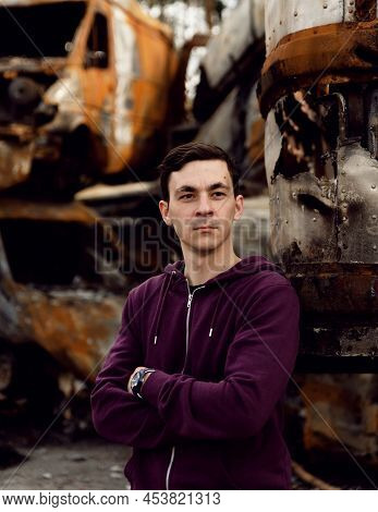Ukrainian Man Stands Against The Background Of Broken And Burnt Cars Affected By Russian Missiles. D