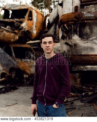 Ukrainian Man Stands Against The Background Of Broken And Burnt Cars Affected By Russian Missiles. D