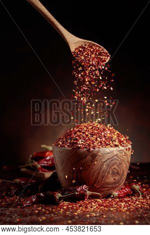Chilli Flakes Are Poured Into A Wooden Dish. Chilli Flakes And Dried Chili Peppers On A Brown Backgr