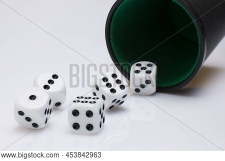Close Up Of Black Cup Tumbler Mug With Green Felt Cover And Five White Dice Rolling Out Of It Showin