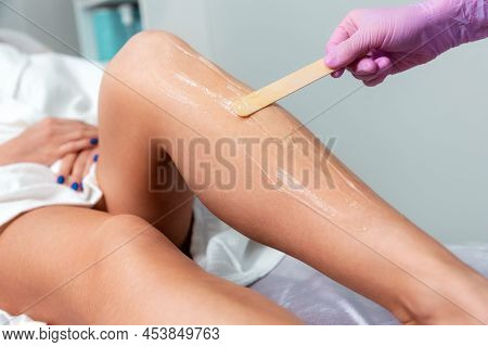 Epilation. Professional Cosmetologist In Pink Medical Gloves Spread Agent Gel To The Client's Leg. T