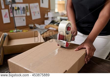 Close-up Of African American Female Worker Of Warehouse Sealing Packed Cardboard Box With Client Ord