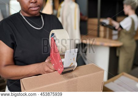 Young Black Woman With Cellotape Sealing Cardboard Box With Packed Goods While Preparing Orders For 