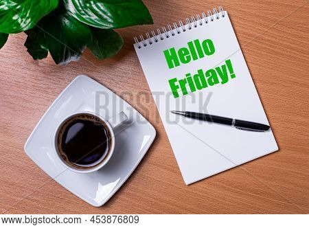 On The Desktop There Is A Green Plant, A White Cup Of Coffee, A Pen And An Open Notepad With The Tex
