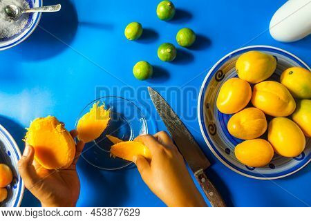 Top View Of The Hand Of A Latin Woman Peeling Mangoes On A Glass Plate And With Traditional Summer F