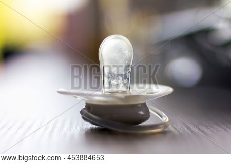 A Close Up Portrait Of A Soother Lying On A Wooden Table Indoor In A Living Room. The Pacifier Is Wh