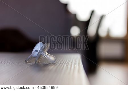 A Portrait Of A Pacifier Lying On A Wooden Table Indoor In A Living Room. The Soother Is White And S
