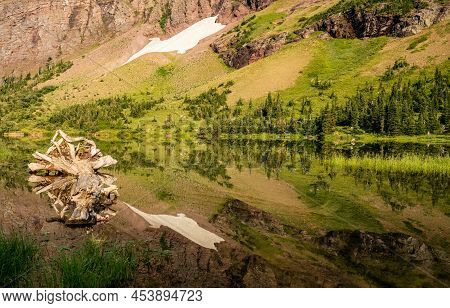 Morning Star Lake Reflects Its Surrounding Mountainside And Snow Field In Glacier National Park