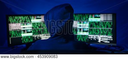 Rear View Od Hooded Hacker By Computer In The Dark Room At Night, Cyberwar Concept.