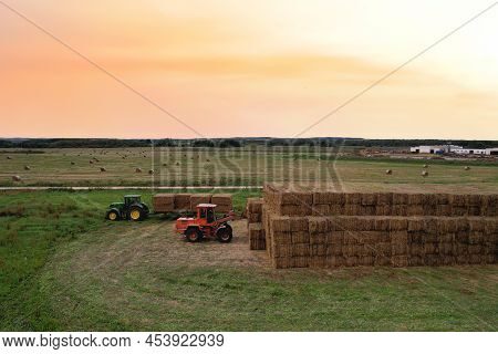 Loader At Unload Round Bales Of Straw From Hay Trailer. Store Hayat Farm. Hay Forage Feed For Beef A