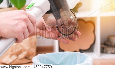 A Man Shakes Out A Trash Container Of A Wireless Vertical Vacuum Cleaner Into A Trash Can. The Conta