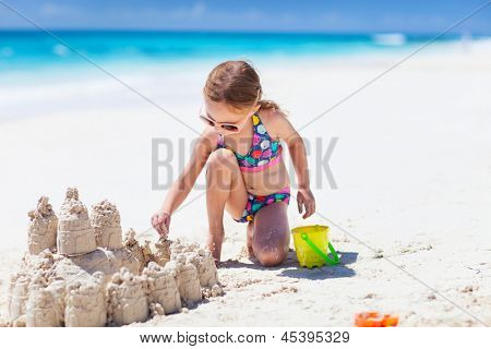 Kleines Mädchen am tropischen Strand machen Sandburg
