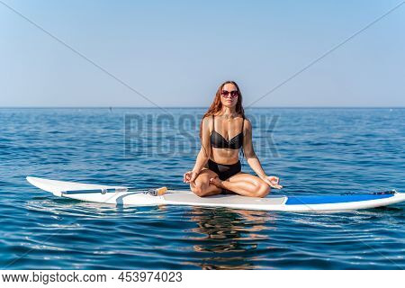 Sporty Girl On A Glanders Surfboard In The Sea On A Sunny Summer Day. In A Striped Swimsuit, He Sits