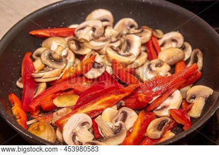 Overhead Shot Of Mushrooms, Red Onions And Red And Yellow Bell Peppers Frying In A Pan With Old Wood